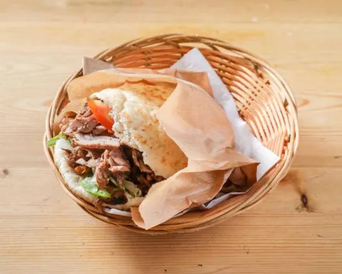 Pita de shawarma rellena de carne asada, lechuga y tomate, en una cesta sobre la mesa de madera