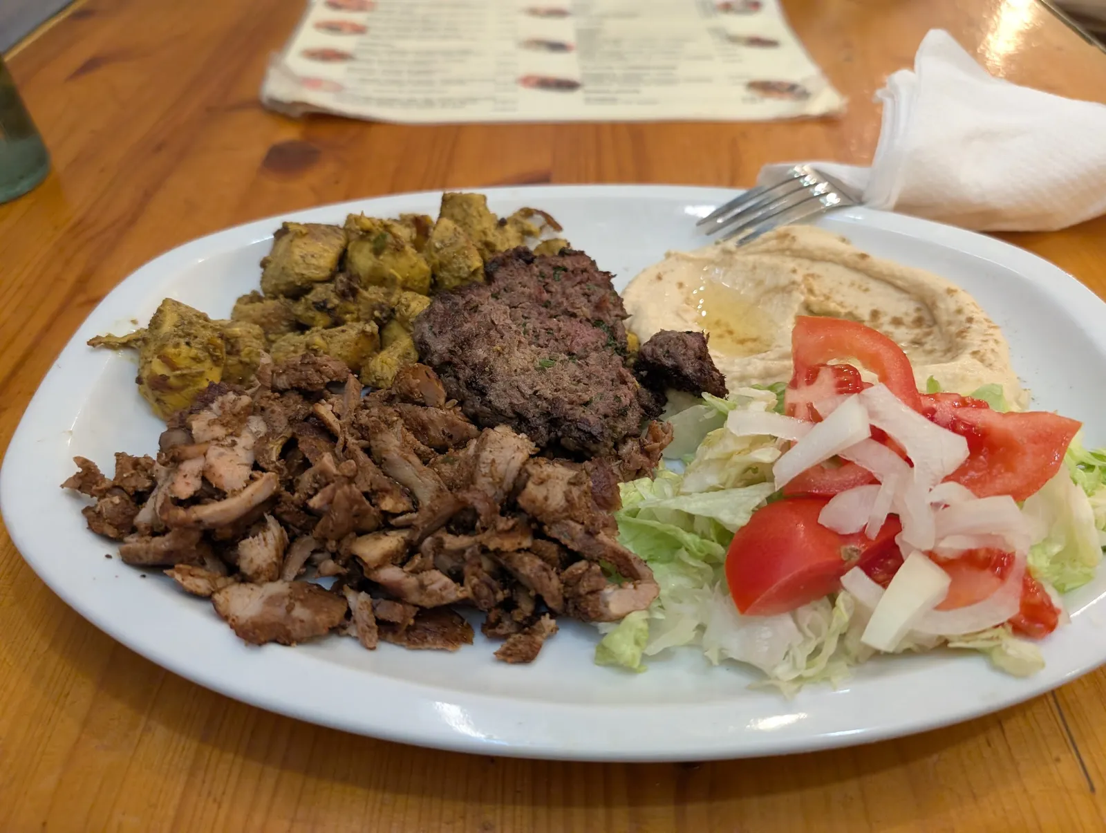 A plate of shawarma, kafta, hummus and tomato and onion salad
